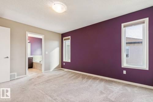 Carpeted room with a ceiling-mounted light fixture, two windows, and a doorway leading to a bathroom featuring a built-in tub with tile surround and a vanity with a dark wood-finish cabinet - 12007 173 Avenue Nw, Edmonton, AB 