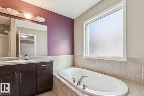 Built-in soaking tub with chrome fixtures, large window with privacy glass, dark wood-finish vanity with countertop, and an integrated basin - 12007 173 Avenue Nw, Edmonton, AB 