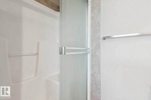 Shower with a frosted glass door, an integrated grab bar, and light-toned wall tiling - 12007 173 Avenue Nw, Edmonton, AB 