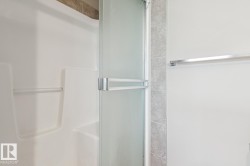 Shower with a frosted glass door, an integrated grab bar, and light-toned wall tiling - 