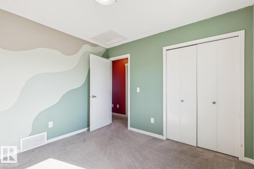 Plush carpet flooring, a wall with decorative wave-patterned paint, a solid white door, and bi-fold closet doors - 12007 173 Avenue Nw, Edmonton, AB 