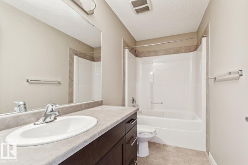 Bathroom featuring a spacious vanity with integrated sink, a full-width mirror, a shower-tub combination, a toilet, and light-toned floor tiling - 12007 173 Avenue Nw, Edmonton, AB 