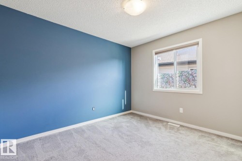 Textured ceiling, carpet flooring, window with white trim, flush mount ceiling light, and blue accent wall - 12007 173 Avenue Nw, Edmonton, AB 
