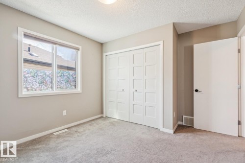 Neutral tone wall paint, textured ceiling, gray carpeting, dual-pane window, and white paneled bi-fold closet doors - 12007 173 Avenue Nw, Edmonton, AB 