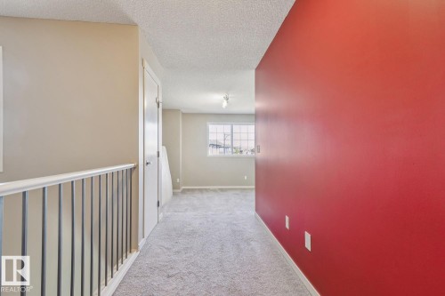 Carpeted hallway featuring a white spindle railing and a window with grid detailing - 12007 173 Avenue Nw, Edmonton, AB 