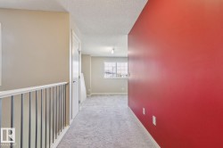Carpeted hallway featuring a white spindle railing and a window with grid detailing - 