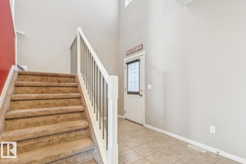 Two-story entryway featuring a carpeted staircase with white banister, tile flooring, and a door with an upper window - 12007 173 Avenue Nw, Edmonton, AB 