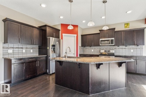 Kitchen featuring dark wood-finish cabinetry, light-colored granite countertops, and a gray subway tile backsplash - 12007 173 Avenue Nw, Edmonton, AB 