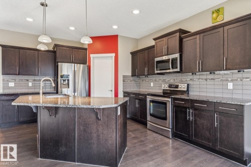 Kitchen featuring dark wood-finish cabinetry, stainless steel appliances, granite countertops, and a central island with a built-in sink - 12007 173 Avenue Nw, Edmonton, AB 
