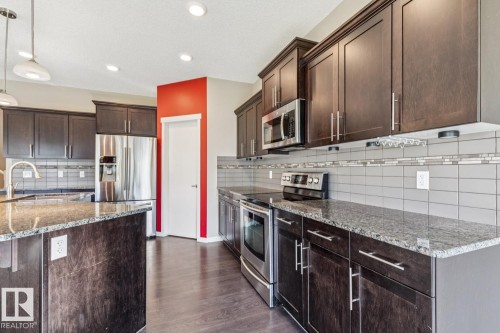 Kitchen featuring dark wood-finish cabinetry, stainless steel appliances, speckled countertops, a tile backsplash with accent tiling, and recessed lighting - 12007 173 Avenue Nw, Edmonton, AB 