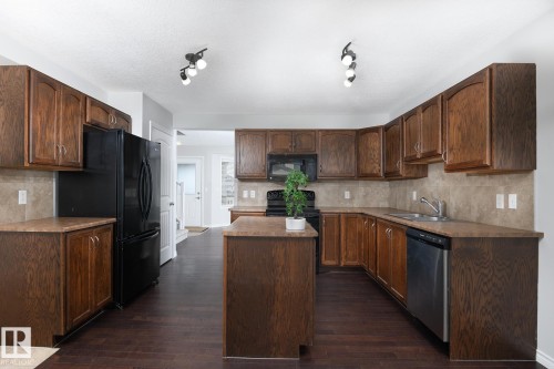 Kitchen featuring wood-finish cabinetry, a central island, a tile backsplash, and dark wood-finish flooring - 441 Songhurst Place, Leduc, AB 