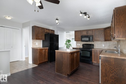 Kitchen featuring wood-finish cabinetry, black appliances, a central island, a tile backsplash, and wood-finish flooring - 441 Songhurst Place, Leduc, AB 