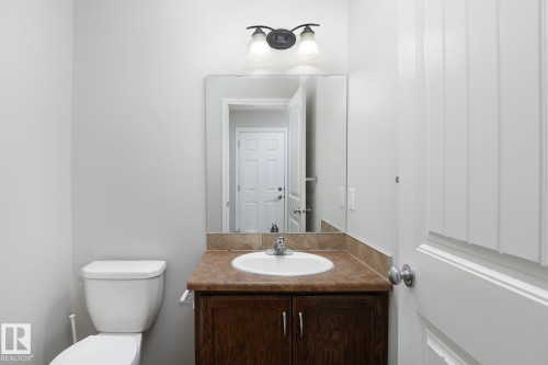 Bathroom featuring a vanity with a white basin, a brown-finish cabinet, and a large wall-mounted mirror - 441 Songhurst Place, Leduc, AB 