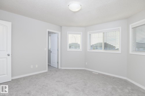 Light gray carpeting and walls, multiple windows with blinds, white trim, and a white interior door - 441 Songhurst Place, Leduc, AB 