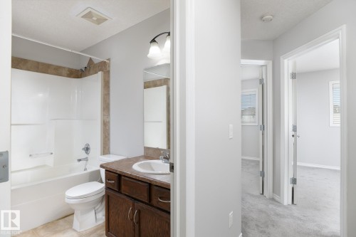 Bathroom featuring a white tub/shower combination with tile surround, wood-finish vanity with an integrated sink, and overhead light fixture - 441 Songhurst Place, Leduc, AB 