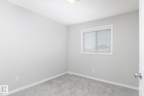 Light gray wall paint, white window frame with blinds, gray carpeting, white trim, and a white interior door - 441 Songhurst Place, Leduc, AB 
