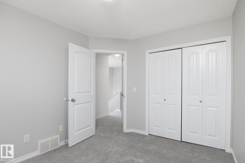 Soft gray wall paint, gray carpeting, white bi-fold closet doors, white interior door, and white trim throughout - 441 Songhurst Place, Leduc, AB 