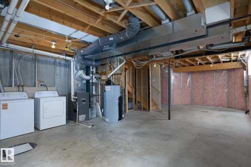 Unfinished basement with exposed wood joists, concrete flooring, and laundry area - 441 Songhurst Place, Leduc, AB 