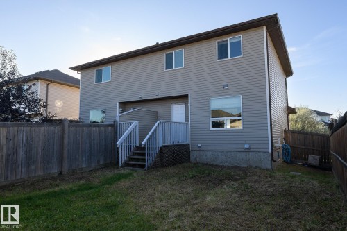 Two-story exterior with neutral siding, a ground-level concrete foundation, and a wooden deck with stairs - 441 Songhurst Place, Leduc, AB 