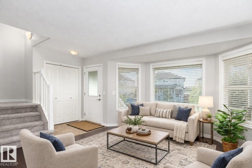 Bay window with multiple panels, staircase with carpeted treads, wood-finish flooring, white paneled entry door with frosted glass, and white bi-fold closet doors - 441 Songhurst Place, Leduc, AB 