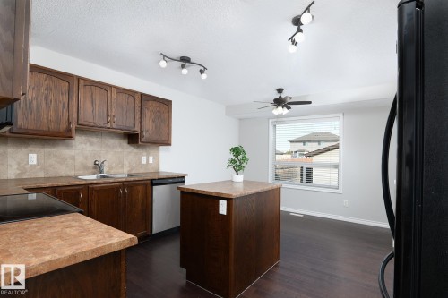 Kitchen featuring wood cabinetry, stone-finish countertops, and a tile backsplash - 441 Songhurst Place, Leduc, AB 