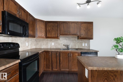 Kitchen featuring wood-finish cabinetry, solid surface countertops, tile backsplash, stainless steel sink, and dark wood-finish flooring - 441 Songhurst Place, Leduc, AB 
