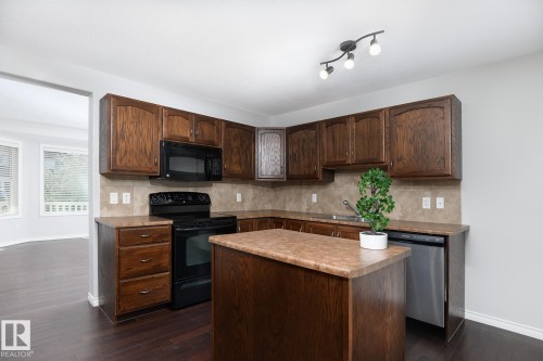 Kitchen featuring wood-finish cabinetry, a built-in microwave, a black range, and a stainless steel dishwasher - 441 Songhurst Place, Leduc, AB 