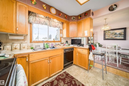 Wood-finish cabinetry, tile flooring, built-in dishwasher, and a window over the sink - 4808 106 Avenue Nw, Edmonton, AB 