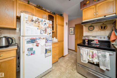 Kitchen featuring wood cabinetry, a built-in range hood, and a stainless steel electric range - 4808 106 Avenue Nw, Edmonton, AB 