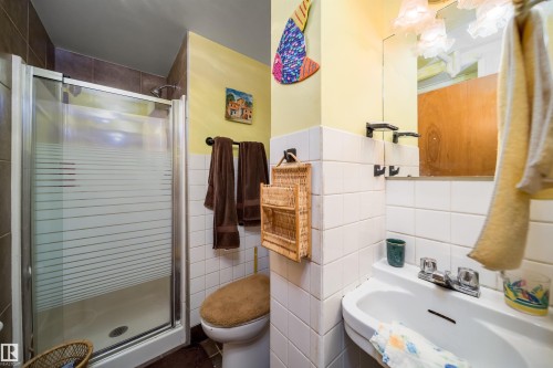Shower enclosure with a sliding frosted glass door, white wall tiling, pedestal sink, and mounted mirror - 4808 106 Avenue Nw, Edmonton, AB 