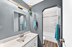 Vanity with integrated sink, modern wall-mounted light fixture, full-width mirror, and a shower-tub combination with wood-finish flooring - 