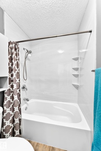Bathtub with integrated shower, chrome fixtures, and a corner shelving unit - 5620 93A Avenue Nw, Edmonton, AB 