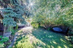 Expansive backyard featuring mature trees, a manicured lawn, and a slatted wood fence - 