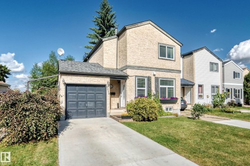Stucco exterior with a pitched shingle roof, attached garage, concrete driveway, and front lawn - 5620 93A Avenue Nw, Edmonton, AB 