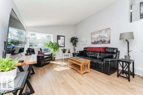 Spacious living area featuring light-toned wood-finish flooring, a large picture window with horizontal blinds, and smooth light-colored walls - 6 Kiniski Crescent Nw, Edmonton, AB 