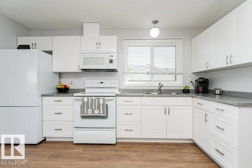 White cabinetry with sleek hardware, wood-finish flooring, white appliances, and a window above the sink - 6 Kiniski Crescent Nw, Edmonton, AB 