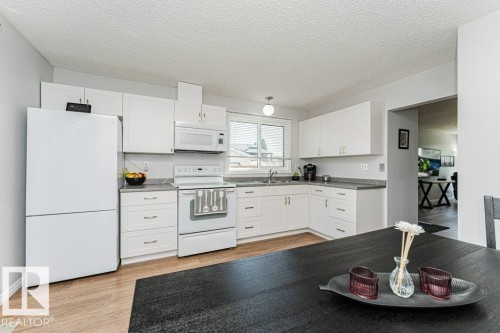 Kitchen featuring white cabinetry, light-toned wood-finish flooring, white appliances, and a window above the sink - 6 Kiniski Crescent Nw, Edmonton, AB 