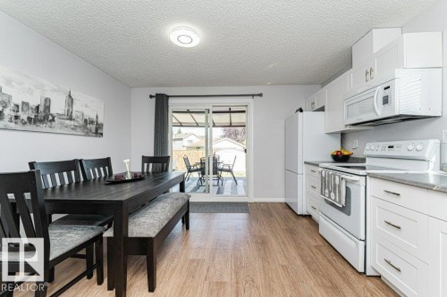 Modern kitchen with white cabinetry, stainless-steel appliances, wood-finish flooring, and sliding glass doors - 6 Kiniski Crescent Nw, Edmonton, AB 