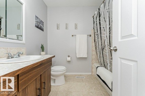 Bathroom featuring a wood-finish vanity with an integrated sink, a built-in tub with tile surround, and a coordinating tile floor - 6 Kiniski Crescent Nw, Edmonton, AB 