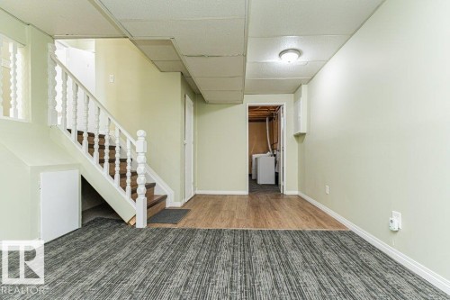 Lower-level space featuring wood-finish flooring, patterned carpeting, and a staircase with white balusters - 6 Kiniski Crescent Nw, Edmonton, AB 