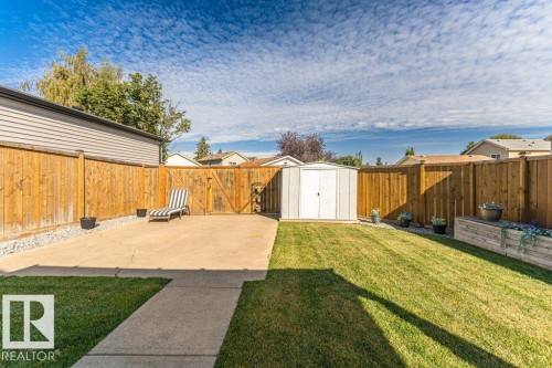 Expansive backyard featuring a manicured lawn, concrete patio, privacy fencing, and a storage shed - 6 Kiniski Crescent Nw, Edmonton, AB 