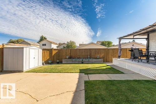 Spacious backyard featuring a slatted wood fence, green lawn, concrete patio, and an elevated deck with lattice skirting - 6 Kiniski Crescent Nw, Edmonton, AB 