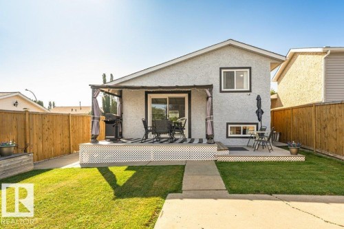 Two-tiered deck with lattice skirting, covered patio area, sliding glass door access, and a manicured lawn - 6 Kiniski Crescent Nw, Edmonton, AB 