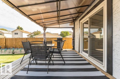 Covered back deck featuring a sliding glass door, wood decking, and a privacy fence - 6 Kiniski Crescent Nw, Edmonton, AB 