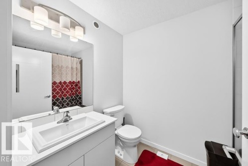 Bathroom featuring a single vanity with integrated sink, chrome faucet, wall-mounted mirror, and contemporary light fixture - 19716 27 Avenue Nw, Edmonton, AB - Indoor Photo Showing Bathroom