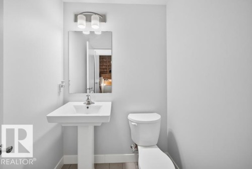 Contemporary powder room featuring a pedestal sink, rectangular mirror, modern vanity lighting, and light wood-finish flooring - 19716 27 Avenue Nw, Edmonton, AB - Indoor Photo Showing Bathroom