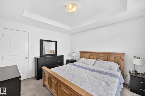 Room featuring a tray ceiling with a flush-mount light fixture, white walls, and neutral carpet flooring - 19716 27 Avenue Nw, Edmonton, AB - Indoor Photo Showing Bedroom