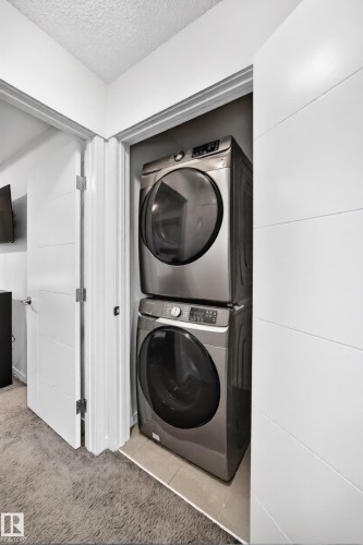 Stackable washer and dryer unit in a dedicated closet with gray wall paint and tile flooring - 19716 27 Avenue Nw, Edmonton, AB - Indoor Photo Showing Laundry Room