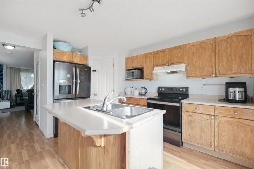 Kitchen featuring wood-finish flooring, wood cabinetry, light-toned countertops, and a central island with an integrated stainless steel sink - 15911 38 Street Nw, Edmonton, AB 