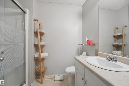 Frosted glass shower enclosure, single vanity with integrated sink, chrome faucet, wall-mounted mirror, and neutral wall paint - 15911 38 Street Nw, Edmonton, AB 